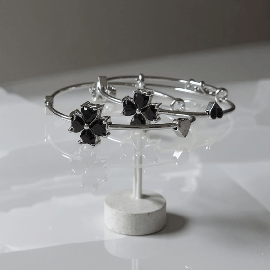 Silver bangles with black flower-shaped ends on a white stand against a light gray background