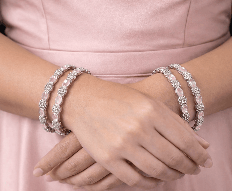 Close-up of hands wearing multiple pearl bracelets on a pink background