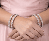 Close-up of hands wearing multiple pearl bracelets on a pink background