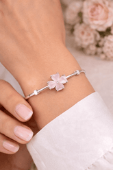 Silver bracelet with pink flower charm on a wrist, with flowers in the background