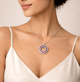 Woman wearing a silver necklace with a circular pendant featuring red stones on a neutral background