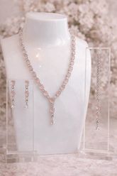 Jewelry set including necklace, earrings, and ring on a mannequin bust with a floral background.