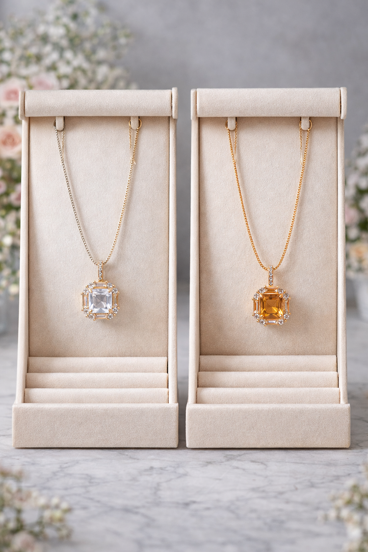 Two gold necklaces with gemstones in display boxes on a marble surface.