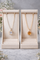 Two gold necklaces with gemstones in display boxes on a marble surface.