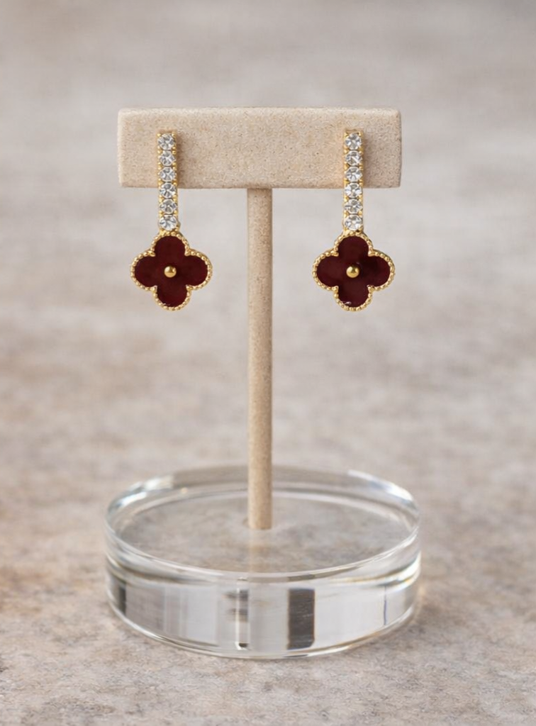 Pair of maroon flower-shaped earrings on a beige stand with a clear circular base.