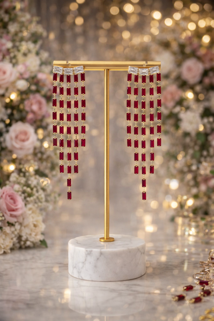 Red and silver checkered earrings on a gold stand with a marble base, against a festive background.