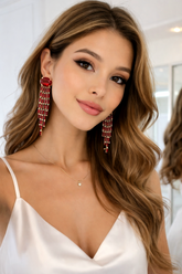 Woman wearing red earrings and a white top with a blurred background