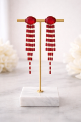 Red beaded earrings on a gold stand with a marble base against a light background