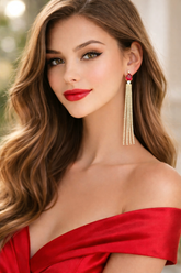 Woman wearing a red off-shoulder top and gold tassel earrings with a blurred background