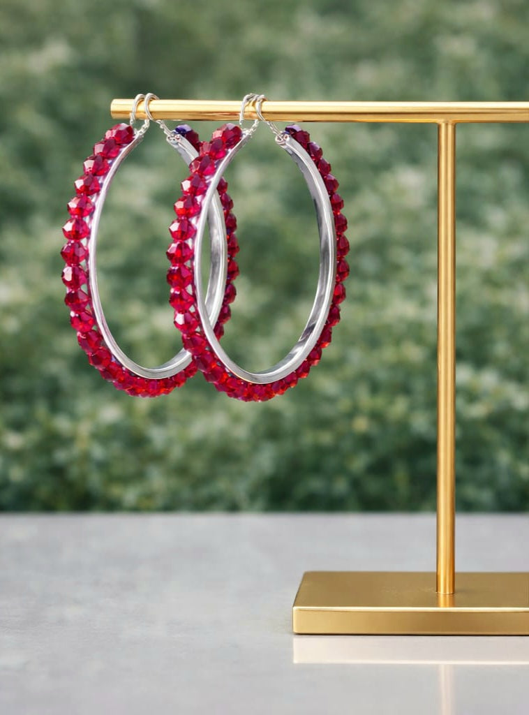 Red beaded hoop earrings on a gold stand with a blurred green background