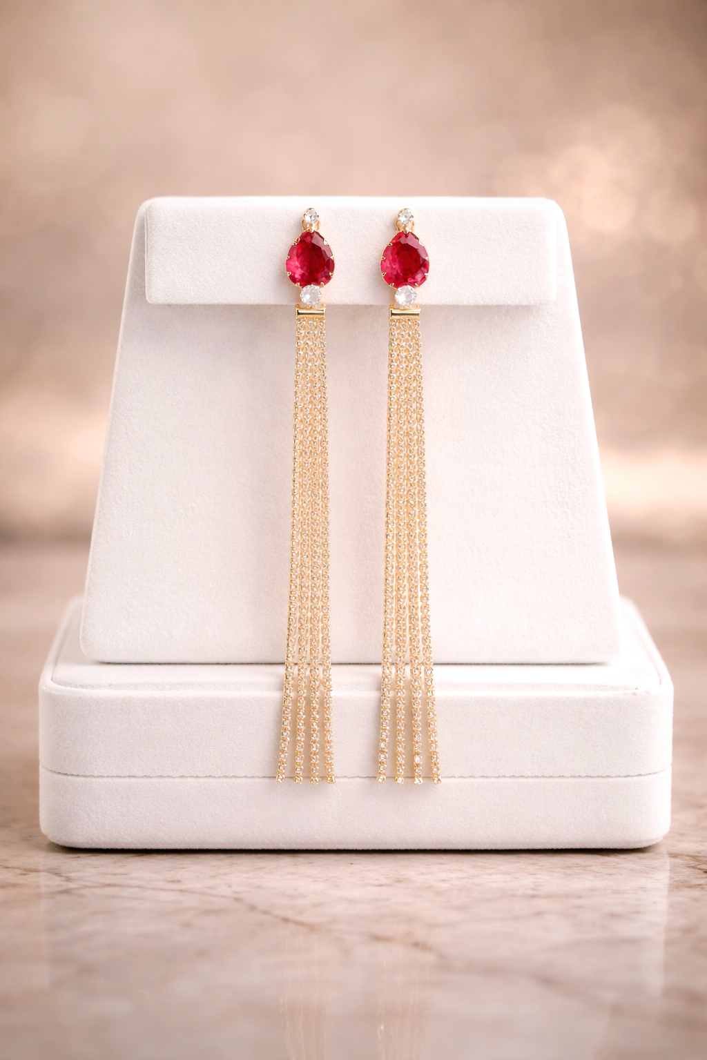 Gold earrings with red stones on a white stand against a beige background