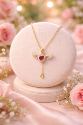 Gold necklace with a red gemstone on a white stand surrounded by pink roses.