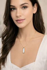 Woman wearing a gold necklace with a pendant against a neutral background
