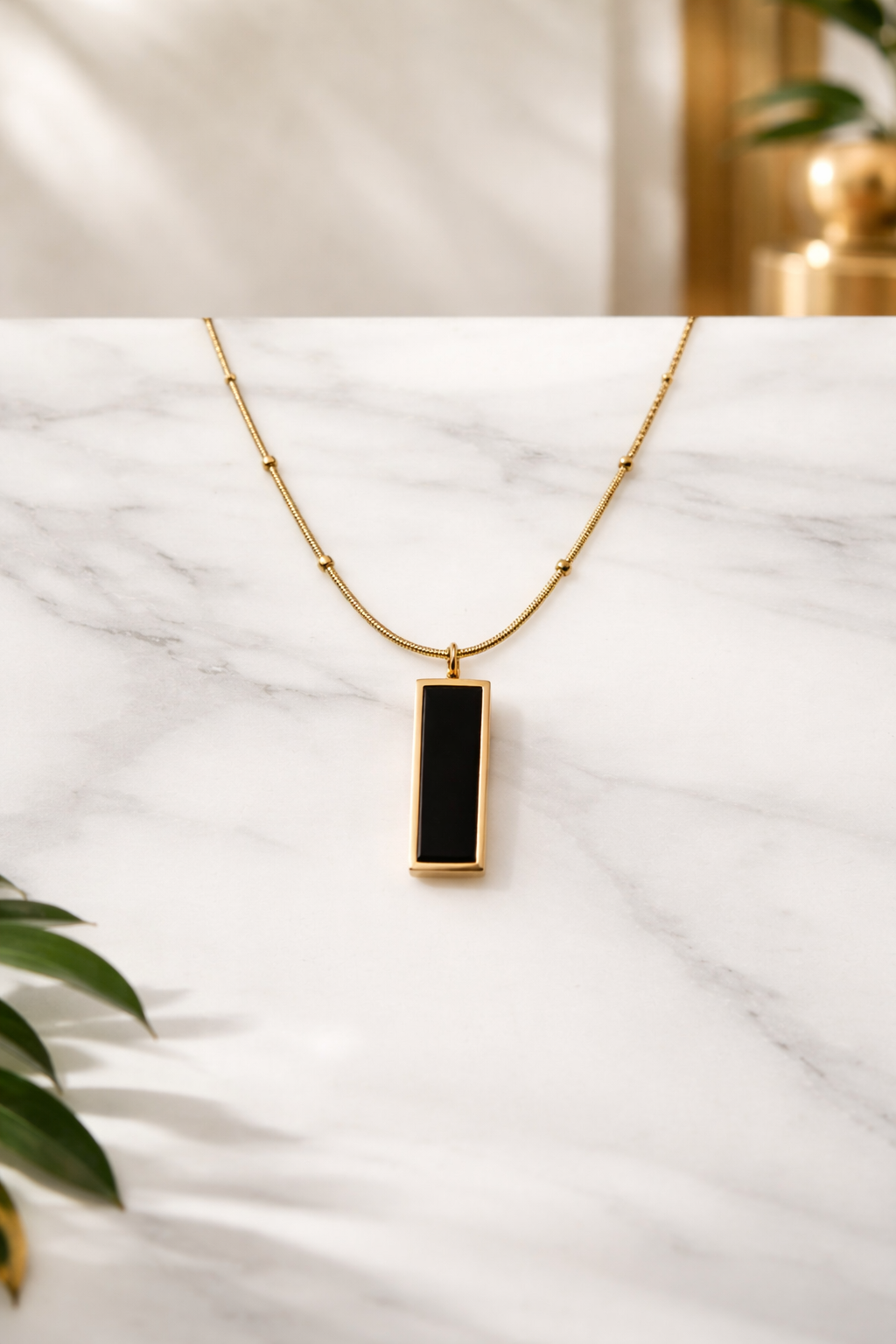 Gold necklace with a black pendant on a marble surface