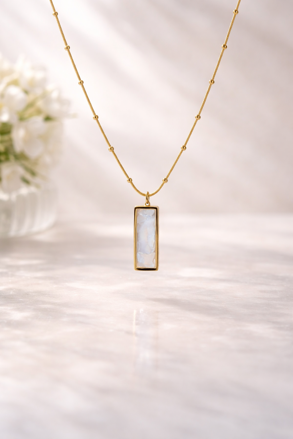Gold necklace with a rectangular pendant on a soft white background