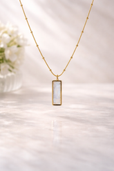 Gold necklace with a rectangular pendant on a soft white background