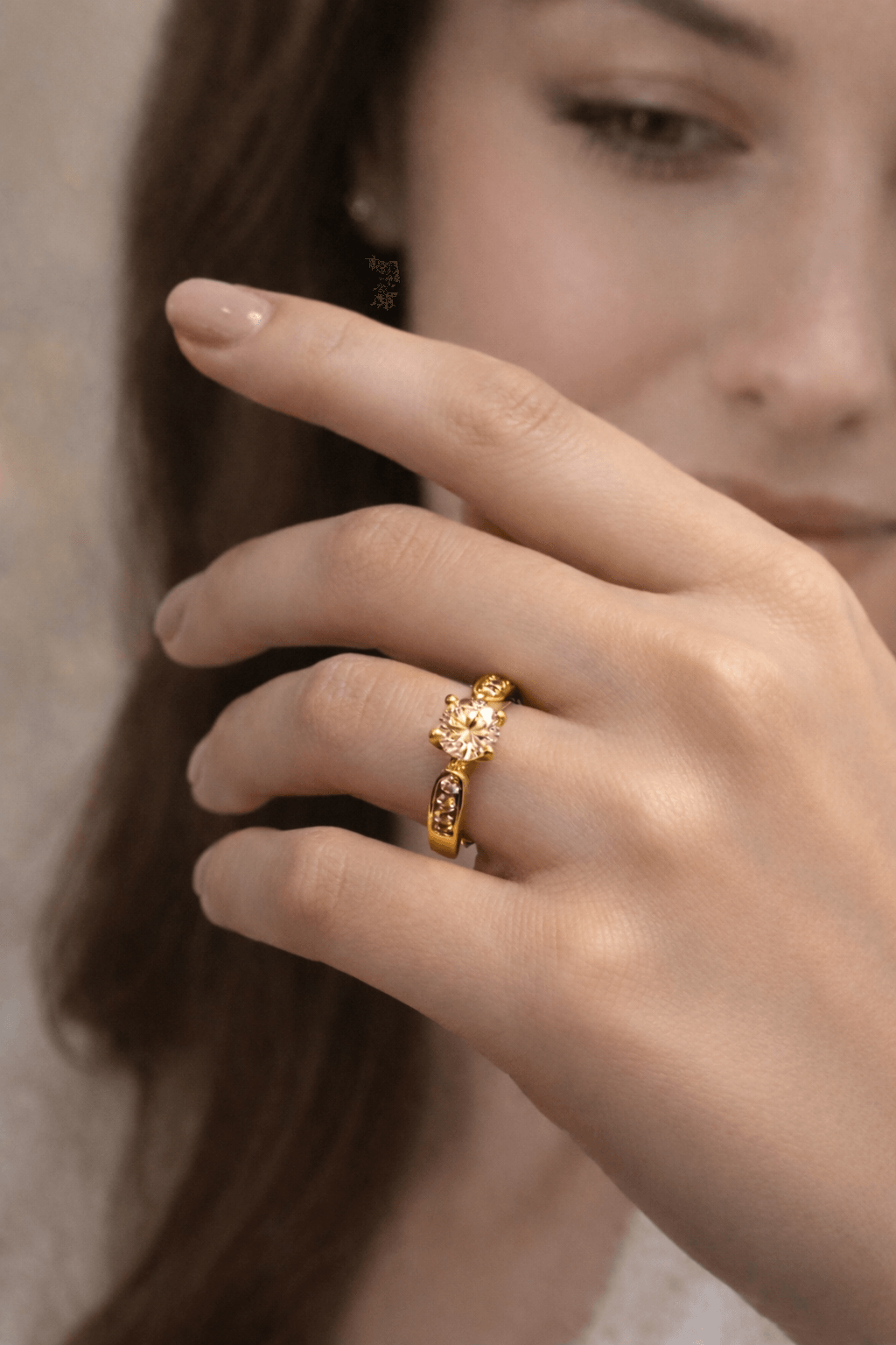 Close-up of a hand wearing a gold ring with a diamond on a neutral background