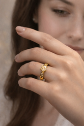 Close-up of a hand wearing a gold ring with a diamond on a neutral background