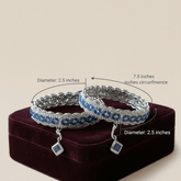 Two silver bracelets with blue stones on a purple stand, showing measurements.