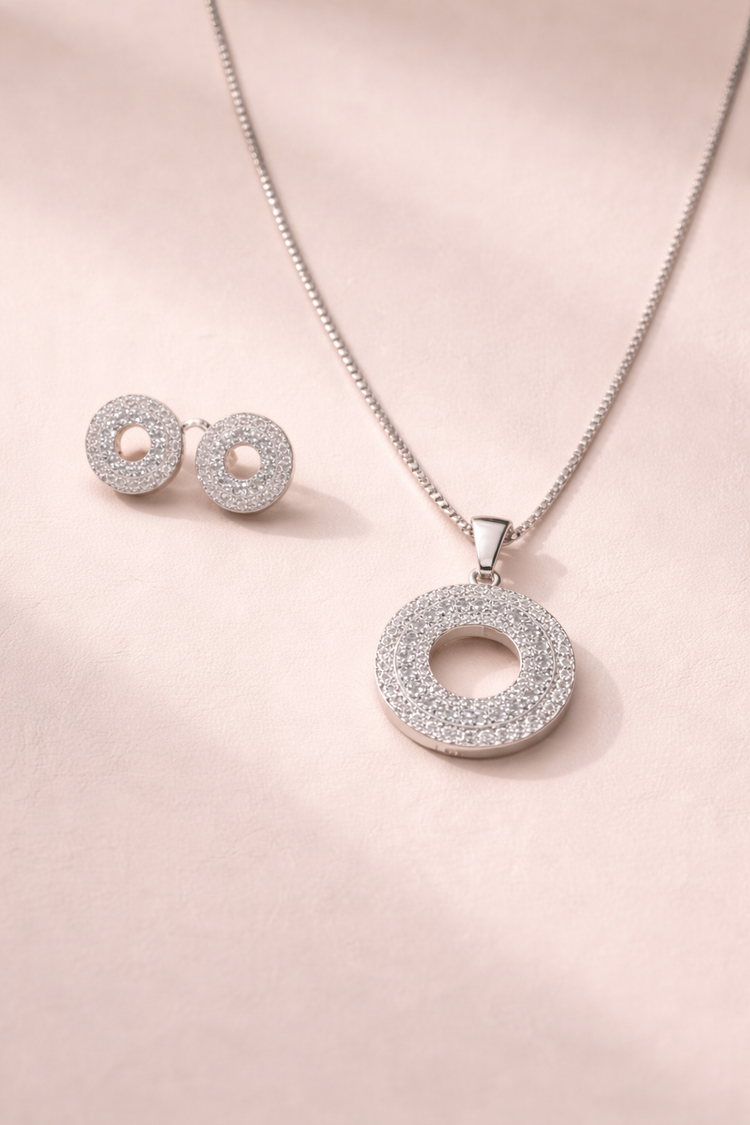 Silver jewelry set with pendant and earrings on a pink background