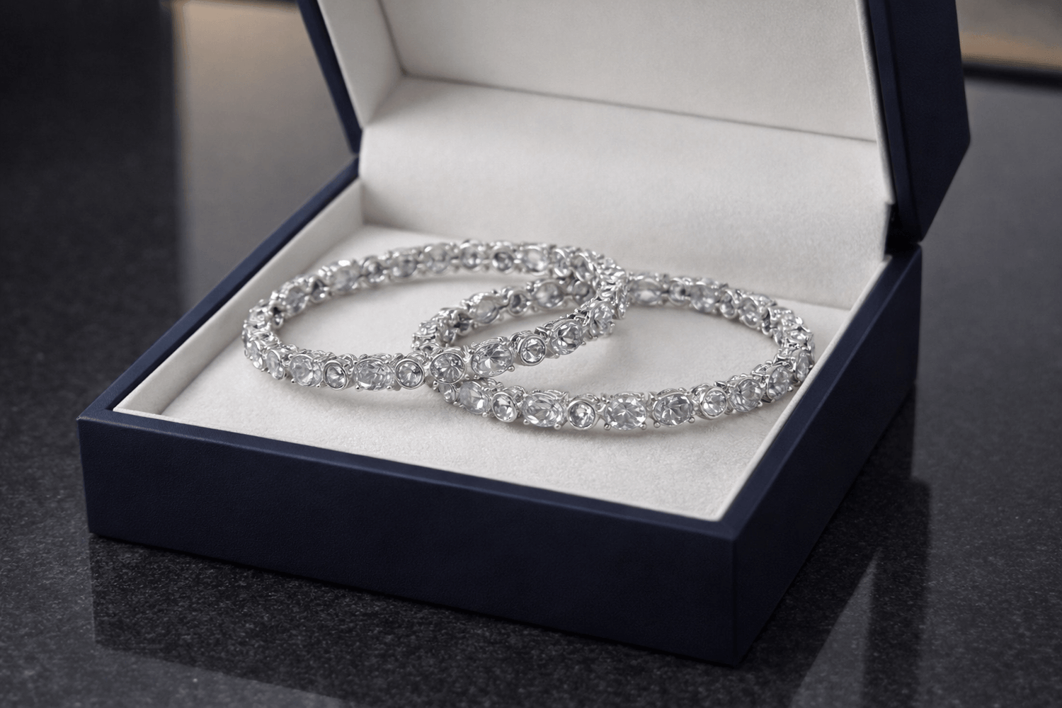 Two silver bracelets in an open jewelry box on a dark surface