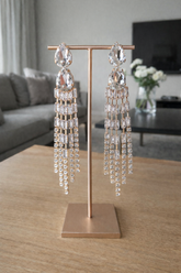 Pair of crystal earrings on a rose gold stand in a living room setting.