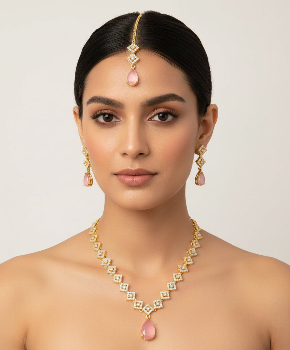 Gold necklace with pink teardrop pendants on a soft gradient background