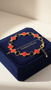Gold bracelet with red clover-shaped charms on a blue jewelry box.