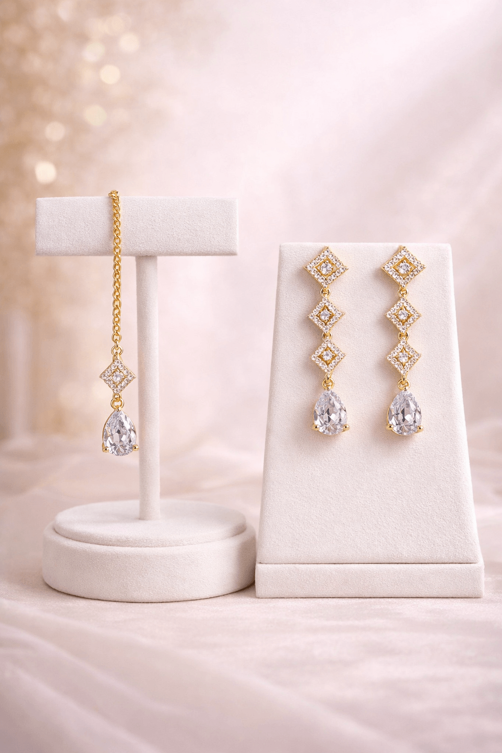 Gold and crystal earrings on a white jewelry stand against a soft pink background