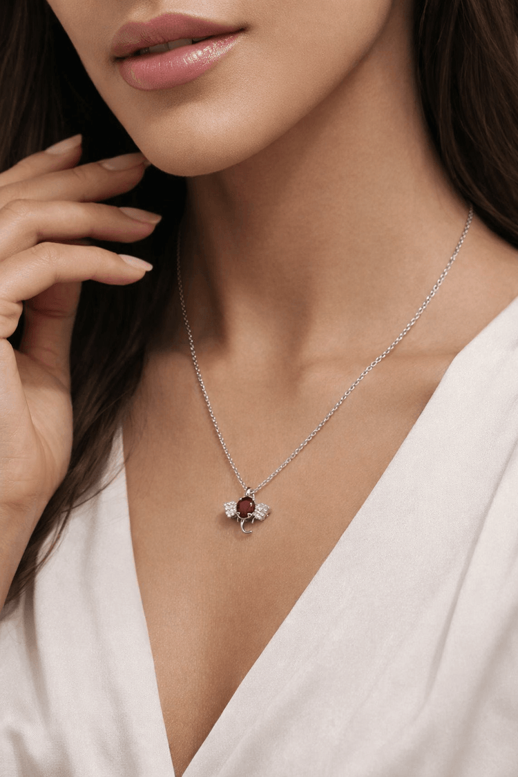 Close-up of a woman wearing a silver necklace with a red gemstone pendant.