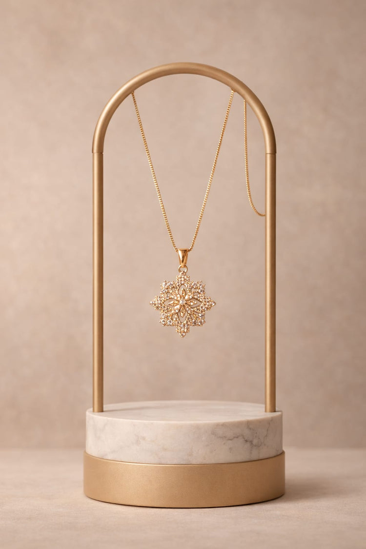 Gold necklace with a floral pendant on a gold and marble stand against a beige background