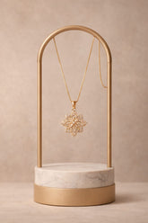 Gold necklace with a floral pendant on a gold and marble stand against a beige background