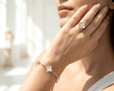 Woman wearing a gold bracelet and ring with white clover-shaped charms.