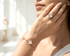 Woman wearing a gold bracelet and ring with white clover-shaped charms.