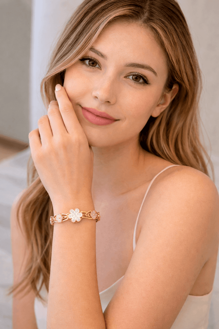 Woman wearing a gold bracelet with a white flower design on a neutral background