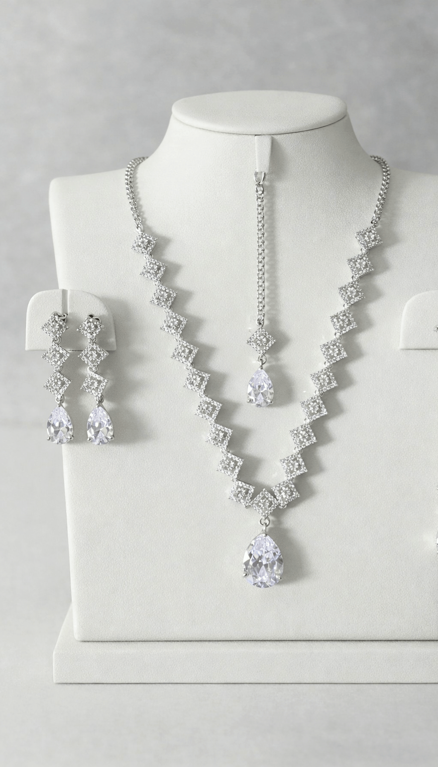 Silver necklace and earrings set on a mannequin bust against a gray background