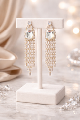 Gold chandelier earrings on a white stand with blurred background