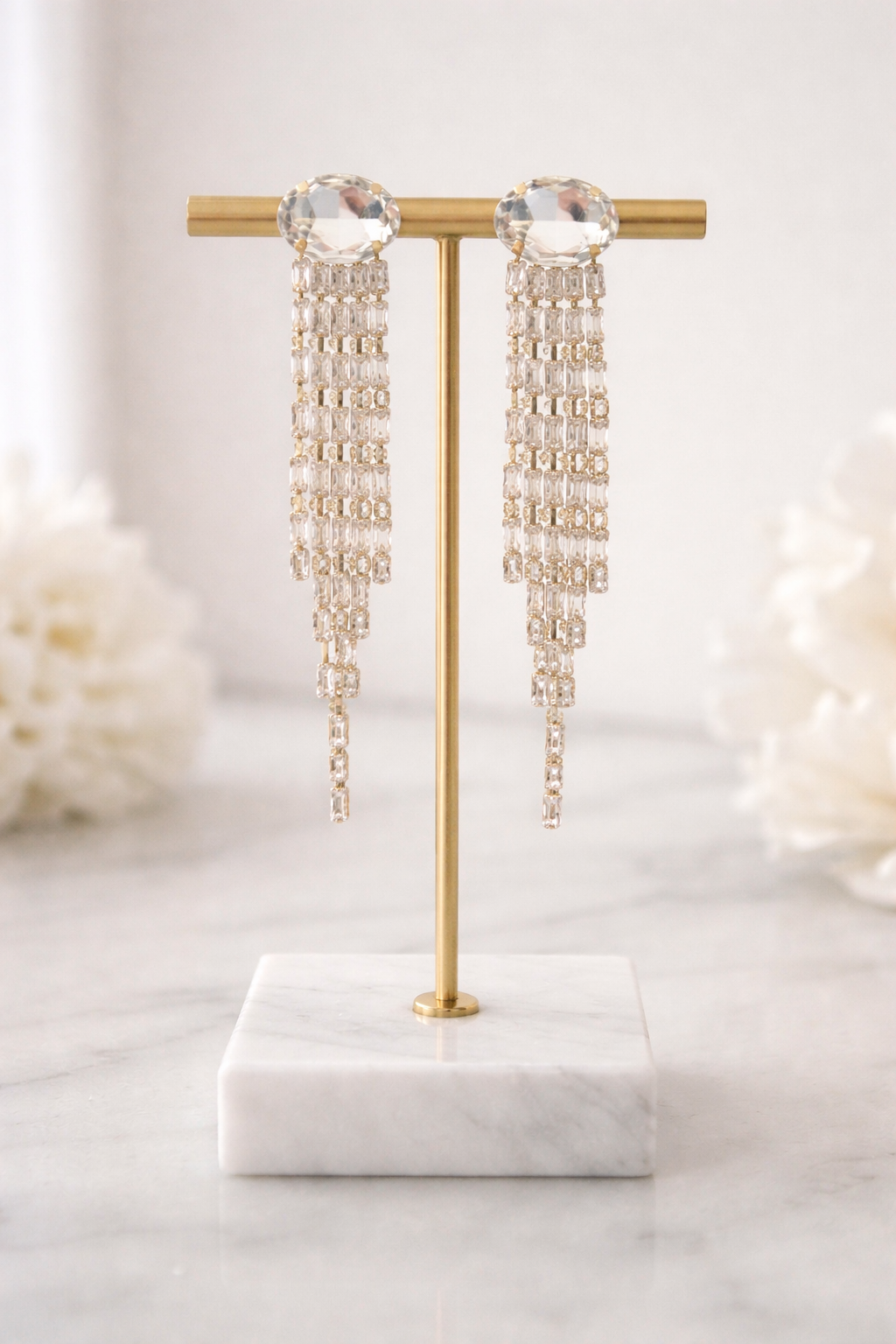 Pair of long, dangling earrings on a gold stand with a marble base.