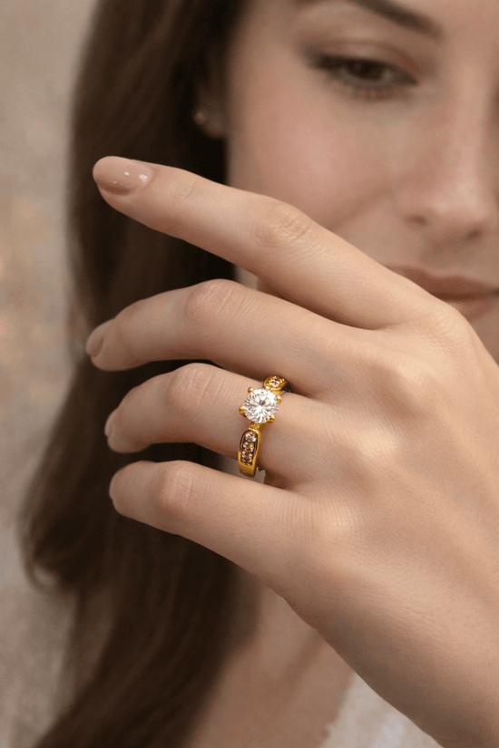 Close-up of a hand wearing a gold ring with a diamond on a blurred background