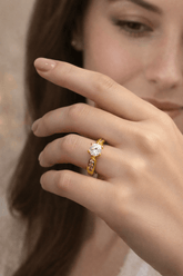 Close-up of a hand wearing a gold ring with a diamond on a blurred background