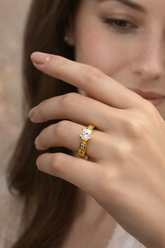Close-up of a hand wearing a gold ring with a diamond on a blurred background