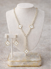 Necklace and earrings with floral designs on a white stand against a gray background