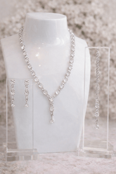 Silver necklace and earrings on a mannequin bust with a blurred floral background