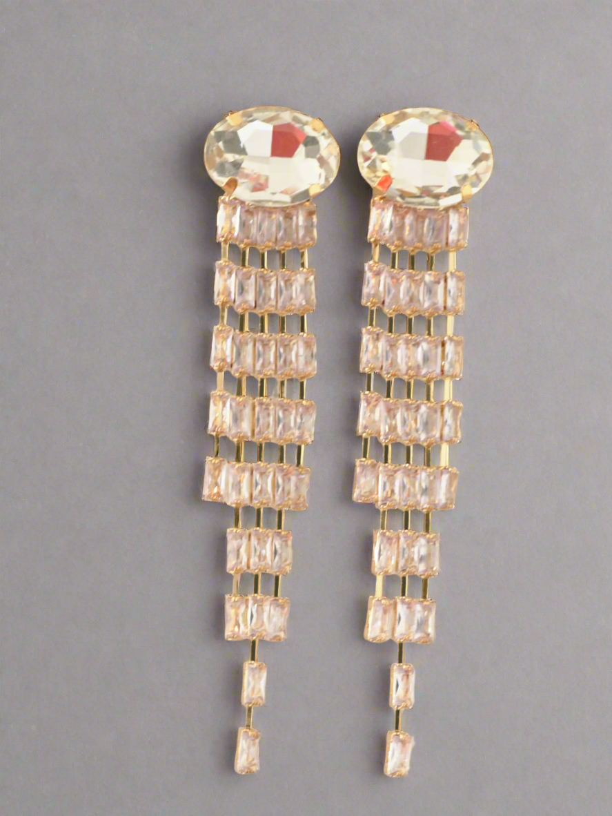 Pair of gold earrings with clear gemstones on a gray background
