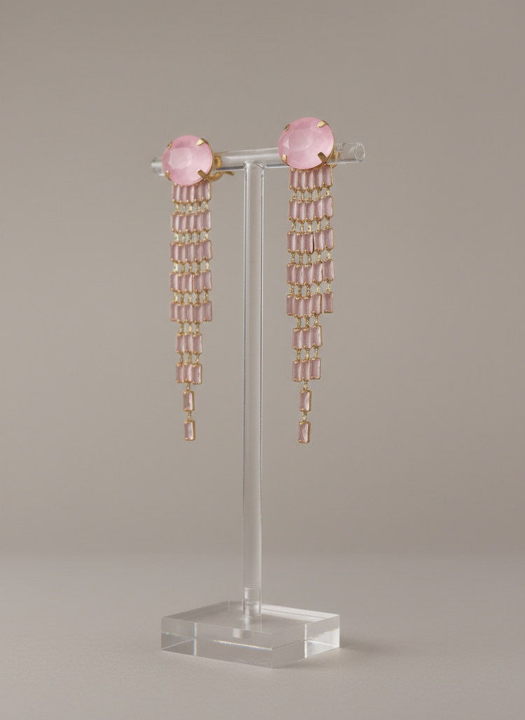 Pair of pink beaded earrings on a clear stand against a beige background