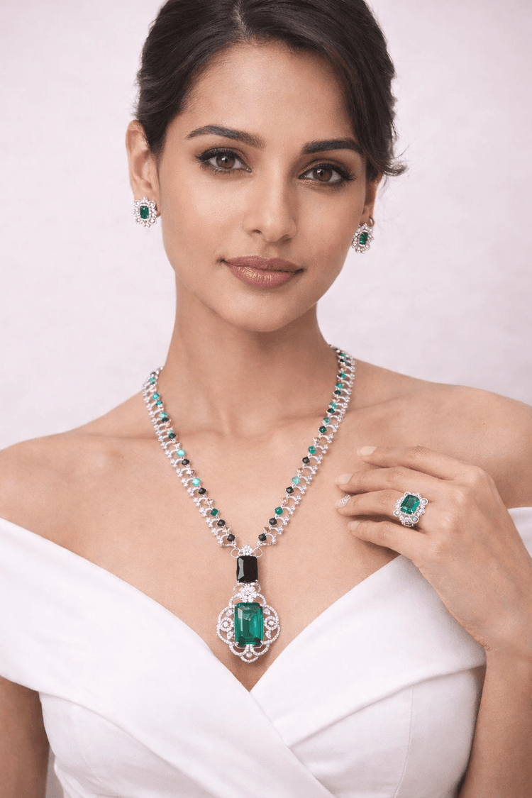 Woman wearing emerald jewelry including a necklace, earrings, and ring on a white background