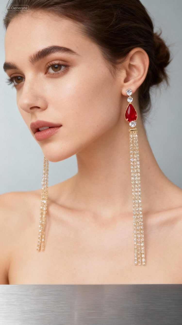 Woman wearing a pair of long, dangling earrings with a red gemstone on a neutral background