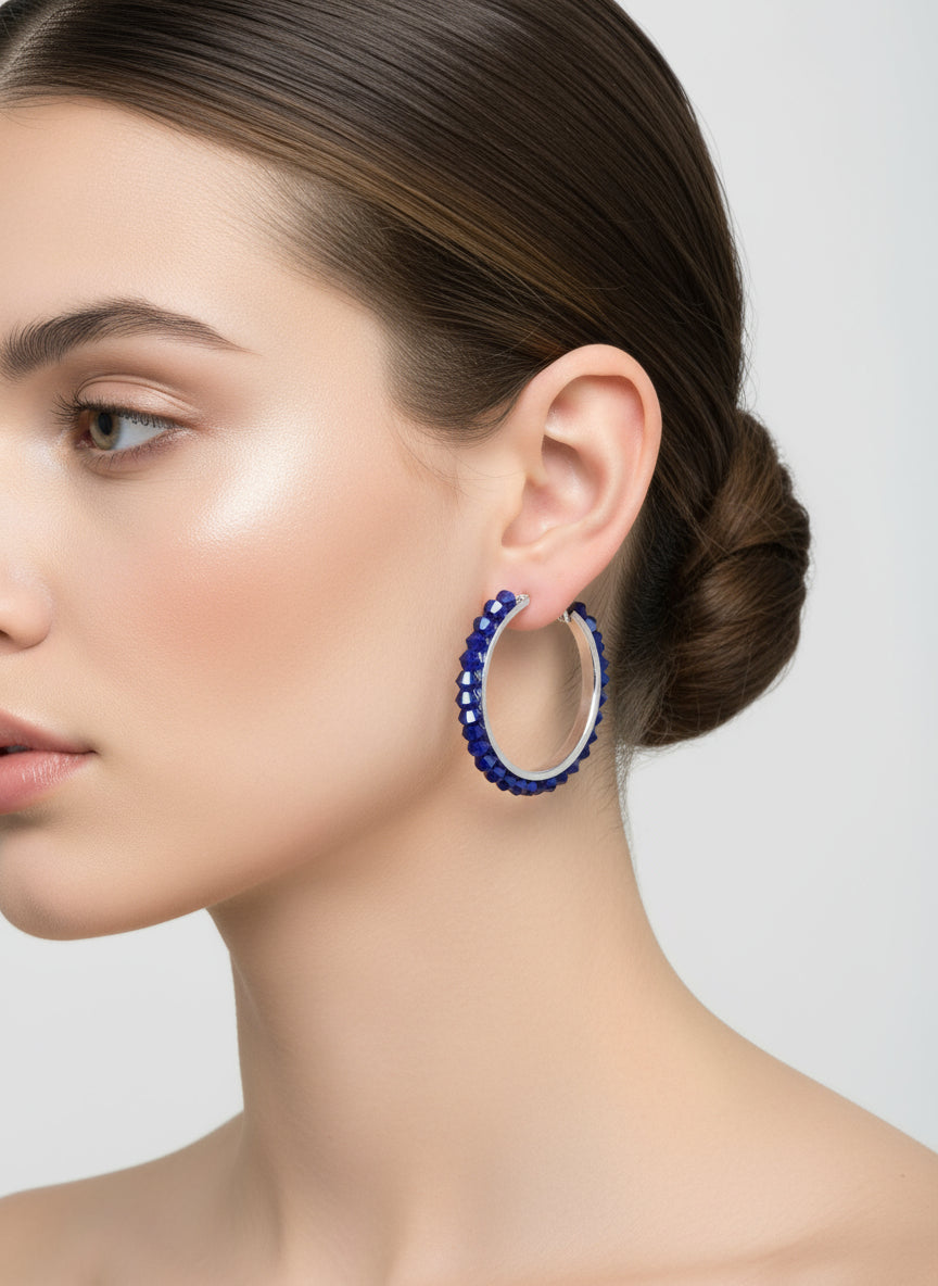 Close-up of a woman wearing blue hoop earrings against a plain background