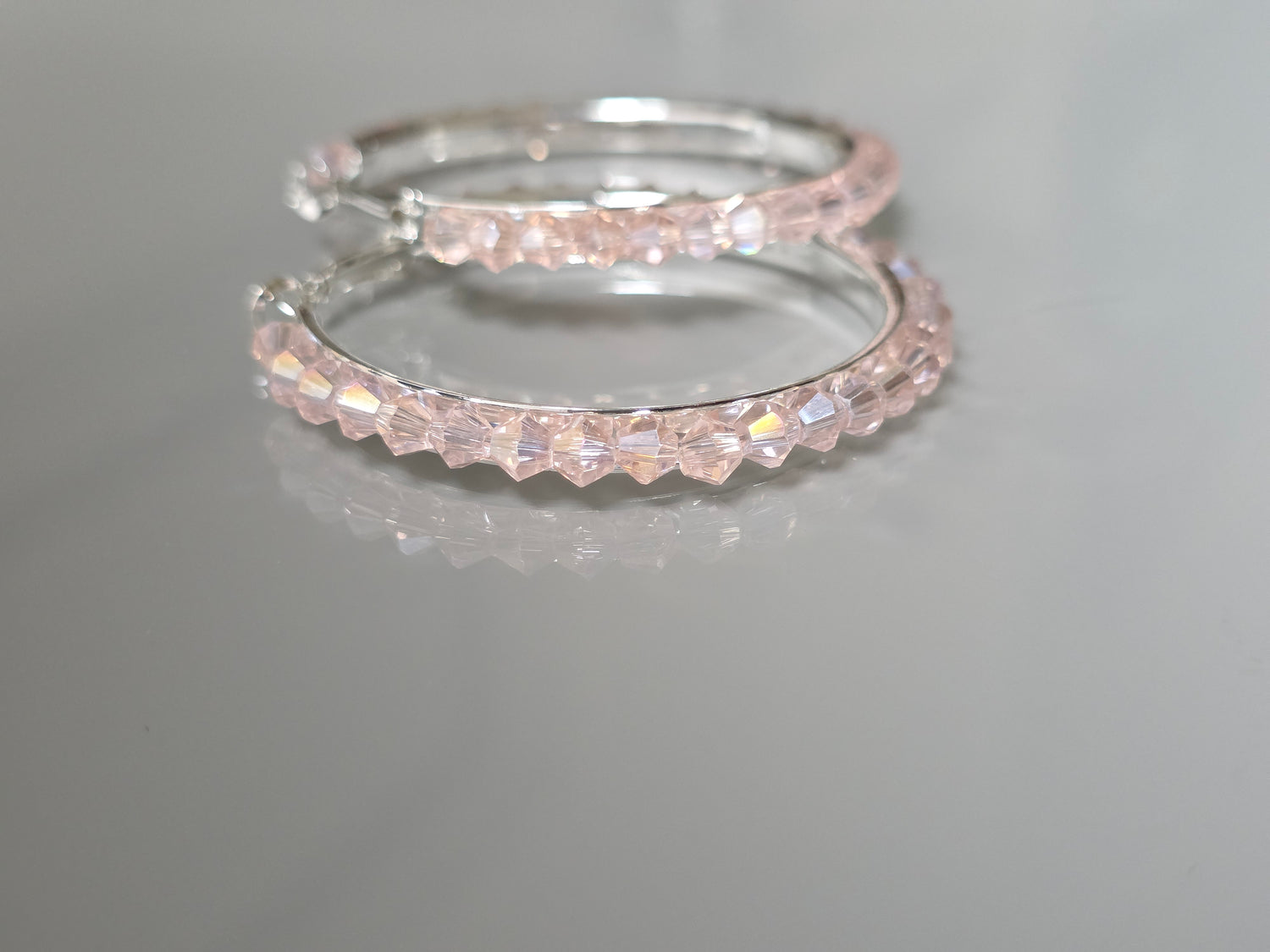 Two silver hoop earrings with clear gemstones on a gray background