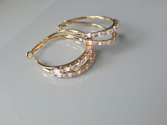Gold hoop earrings with clear gemstones on a gray background